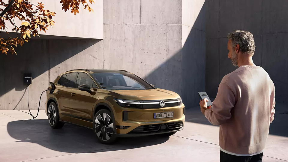 Der neue Tiguan direkt an der Wallbox während der Fahrer über sein Smartphone den Ladestand checkt Der neue Tiguan direkt an der Wallbox während der Fahrer über sein Smartphone den Ladestand checkt